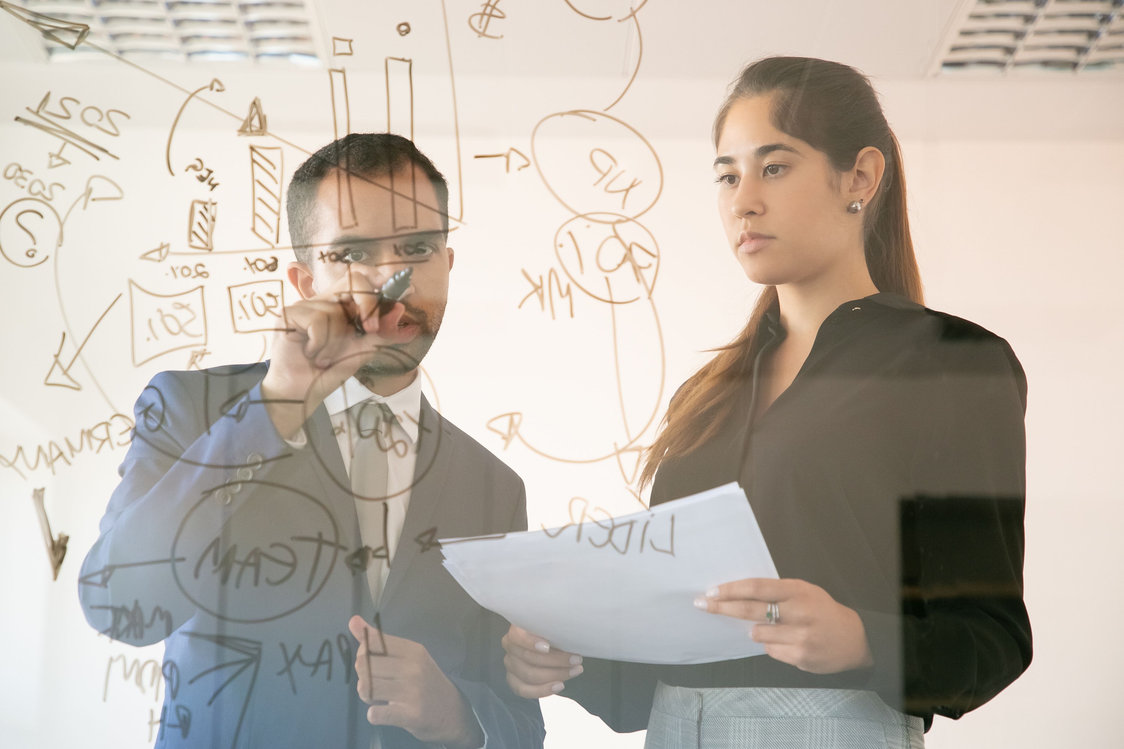 content-african-american-manager-writing-chart-glass-board-professional-young-pretty-female-colleague-holding-document-looking-graph-conference-room-teamwork-marketing-concept.jpg?1741195500827