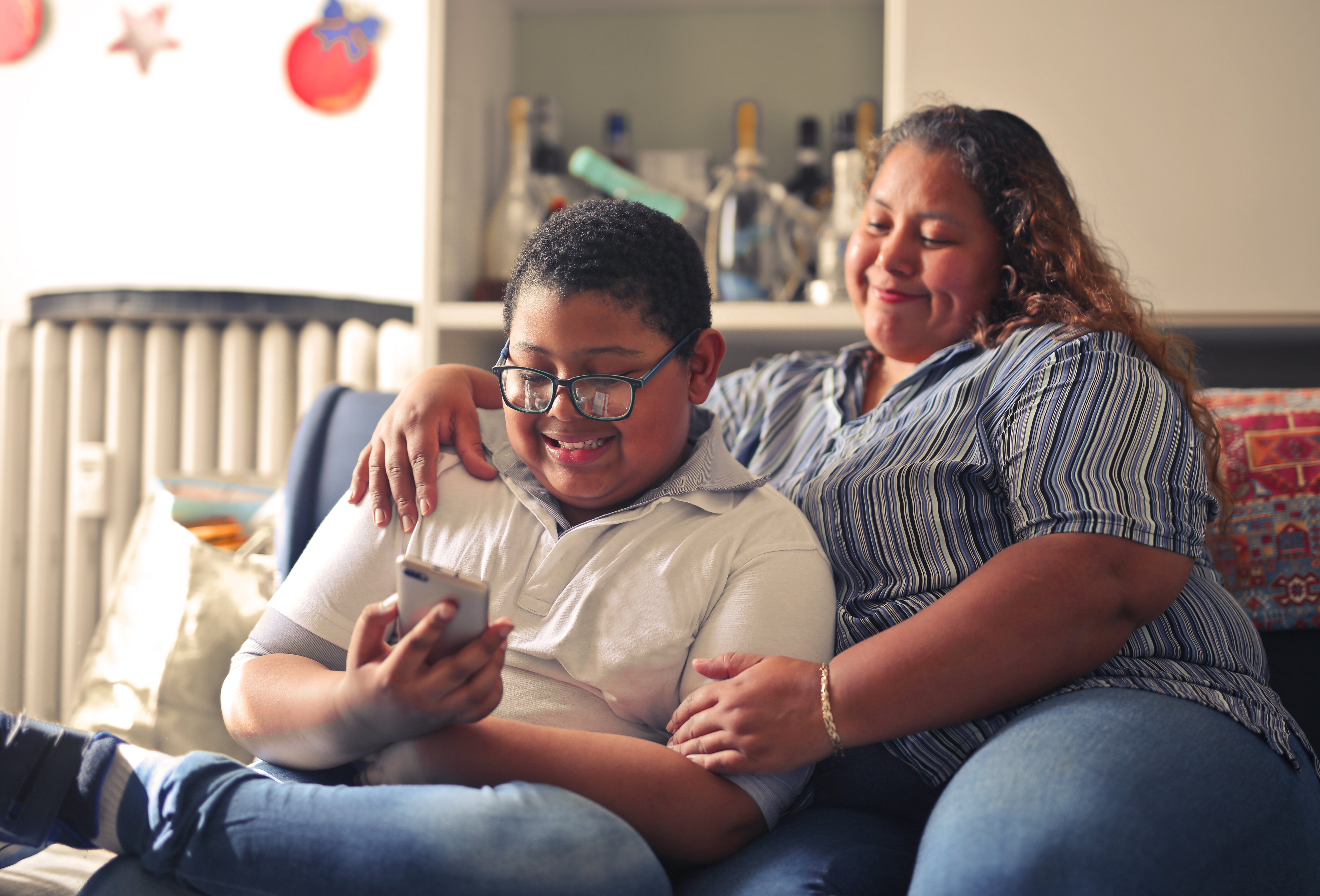 madre-hispana-y-su-hijo-trabajando-con-un-telefono-inteligente-sentados-en-el-sofa.jpg?1746806774483